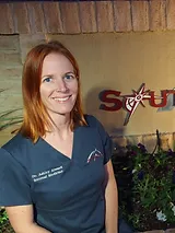 Dr. Ashley Alward, DVM, DACVIM, CVA, smiles while standing in front of a sign with flowers in the foreground - Southwest Equine Veterinary